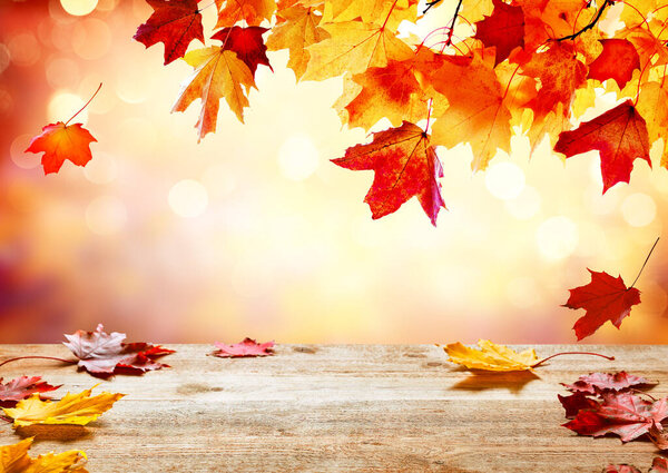 Wooden table top on blur autumn background. Autumn golden abstract background with bokeh light and colorful leaves. Beautiful autumn leaves falling on wooden surface.