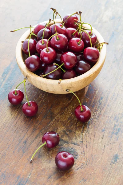 Cerejas vermelhas frescas em tigela em uma mesa de madeira — Fotografia de Stock