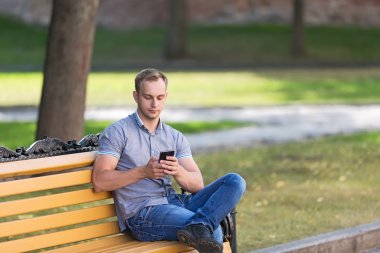 Bir akıllı telefon ile parkta oturan genç adam 