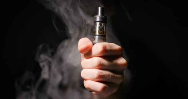 Ηλεκτρονικό τσιγάρο που αρπάζεται από αρσενικό χέρι σε σκούρο φόντο και ατμό — Αρχείο Βίντεο