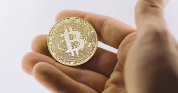 Inspecting shiny physical bitcoin against white background — Stock Video