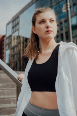 Eşofmanlı genç bir kız şehre karşı merdivenlerde duruyor.