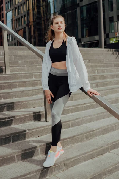 A young girl in a tracksuit stands on the stairs against the city — Stock Photo, Image