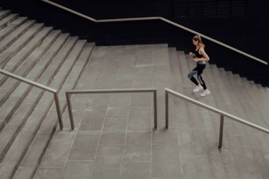 Eşofmanlı genç bir kız merdivenlerden yukarı koşuyor, bir iş merkezinde.