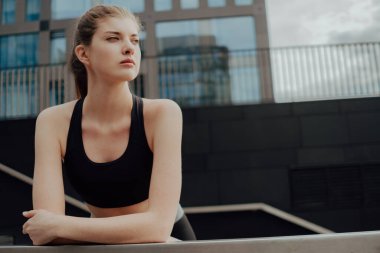 Eşofmanlı genç bir kız şehre karşı merdivenlerde duruyor.