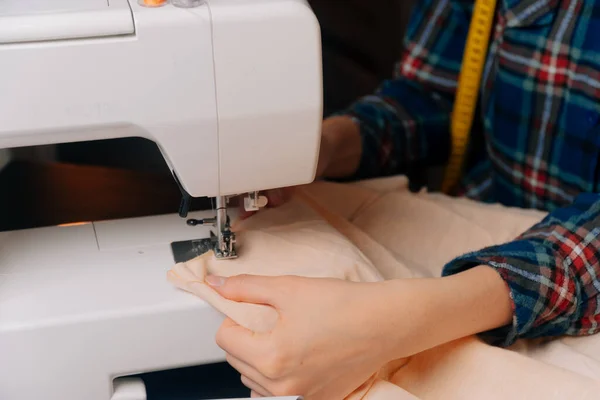 A costureira insere o pano sob a máquina de costura para o overlock. Uma visão de close-up de mãos de mulheres que mantêm um esboço da costura — Fotografia de Stock