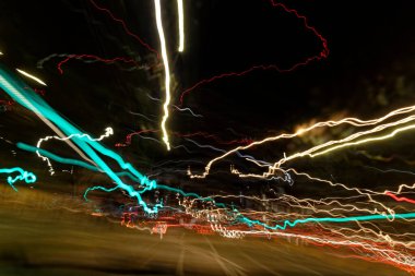 Uzun pozlama ışık yolları soyut kentsel arka plan olarak gösterilir. Çok renkli sokak fenerlerinin ve geçmekte olan arabaların farklı ışık yolları var. Karanlık, uzun süreli kentsel arka planda dağılıyorlar..