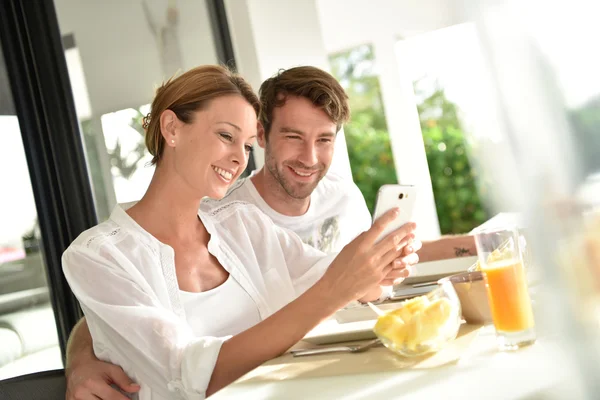 Couple using smartphone at breakfast time — Stock Photo, Image