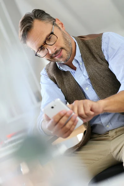 Ο άνθρωπος που κάθεται στο γραφείο χρησιμοποιώντας smartphone — Φωτογραφία Αρχείου