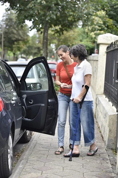 Opiekun, pomagając kobieta wychodzi w samochodzie — Zdjęcie stockowe