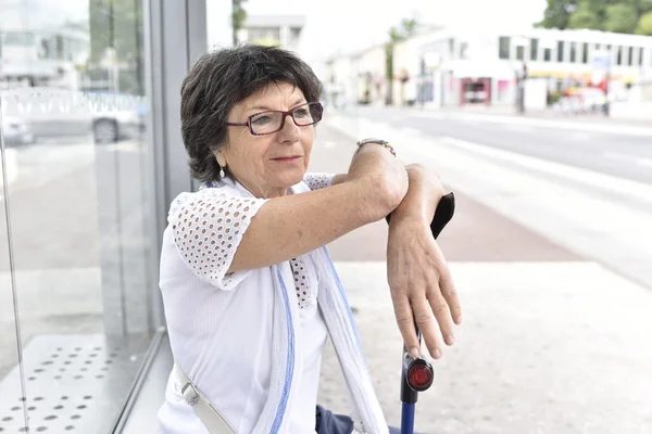 Kvinna med krycka väntar vid busshållplatsen — Stockfoto