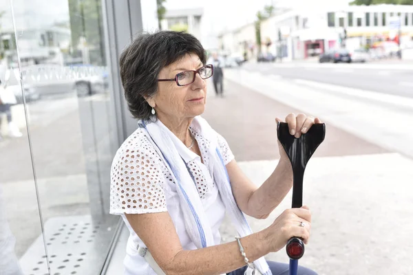 woman with crutch waiting at bus stop