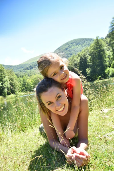 Mãe e filha deitada junto ao lago — Fotografia de Stock