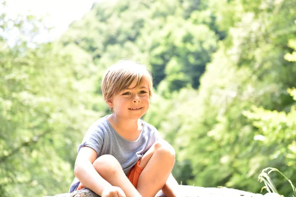 Χαριτωμένο μικρό αγόρι που κάθεται σε βράχο — Φωτογραφία Αρχείου