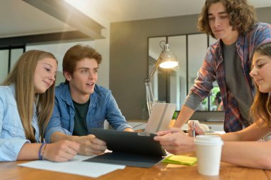 Proje üzerinde çalışmak için masanın etrafında toplanan genç öğrenciler