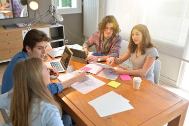 Proje üzerinde çalışmak için masanın etrafında toplanan genç öğrenciler