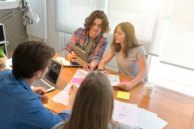 Proje üzerinde çalışmak için masanın etrafında toplanan genç öğrenciler