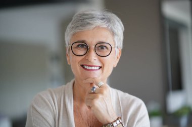 55 yaşında, beyaz saçlı, gülümseyen çekici bir kadının portresi.