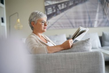Gazete okuyan yaşlı bir kadın, kanepede rahatlamış.