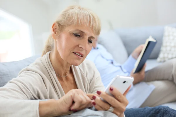 Woman using smartphone, husband reading book — Stock Photo, Image