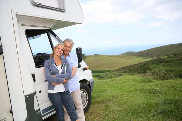 Casal em pé por motorhome no campo — Fotografia de Stock