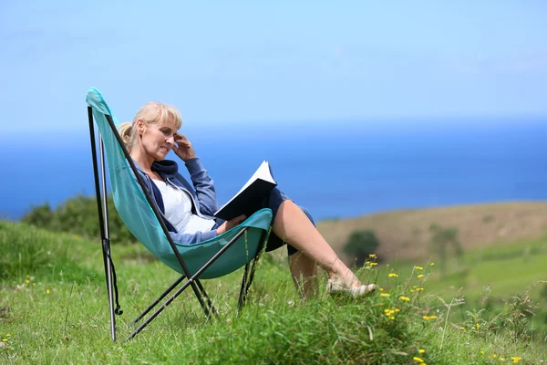 Frau liest Buch auf einem Hügel am Meer — Stockfoto