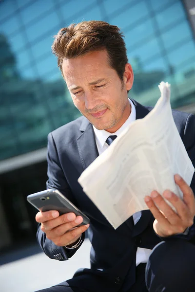 Geschäftsmann mit Smartphone und Zeitung — Stockfoto