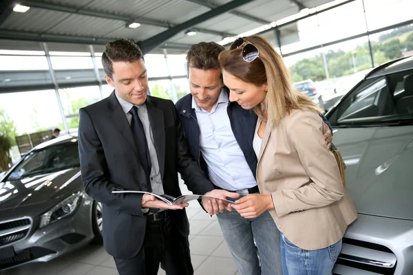 Couple in car dealership looking at brochure — Stock Photo, Image