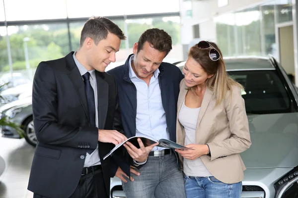 Couple in car dealership looking at brochure — Stock Photo, Image