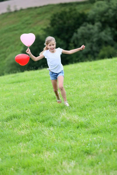 Liten flicka kör i fältet med ballonger — Stockfoto