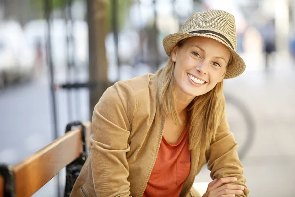 Mulher sorridente sentada no banco público — Fotografia de Stock