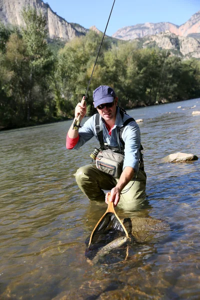 Pêcheur attrapant la truite fario dans la rivière — Photo
