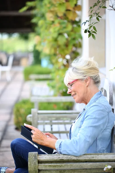 Senior woman reading book on bench — Stock Photo, Image