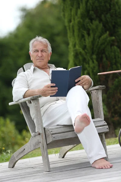 Hombre leyendo libro en silla de la cubierta de la piscina — Foto de Stock