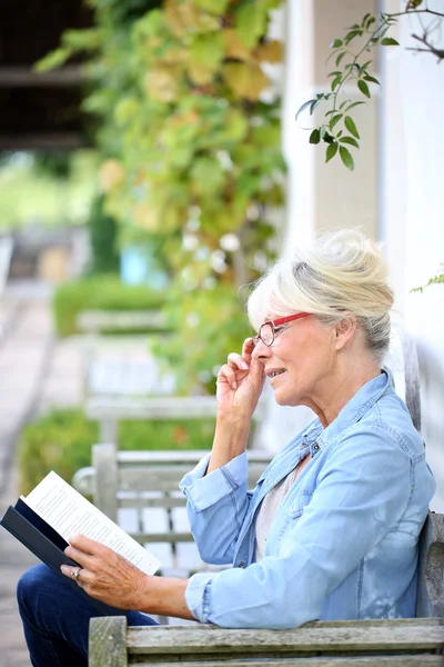 Senior woman reading book on bench — Stock Photo, Image