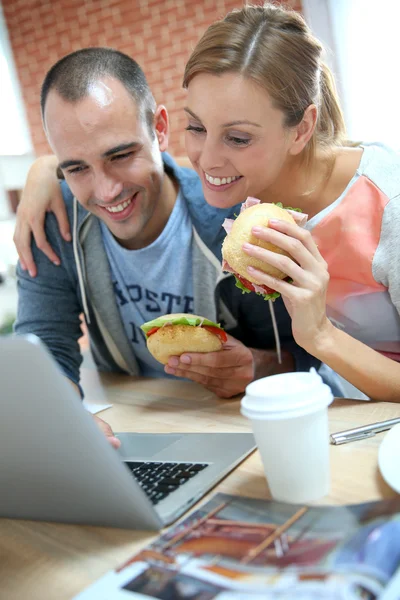 Roommates eating sandwich in front of laptop — Stock Photo, Image