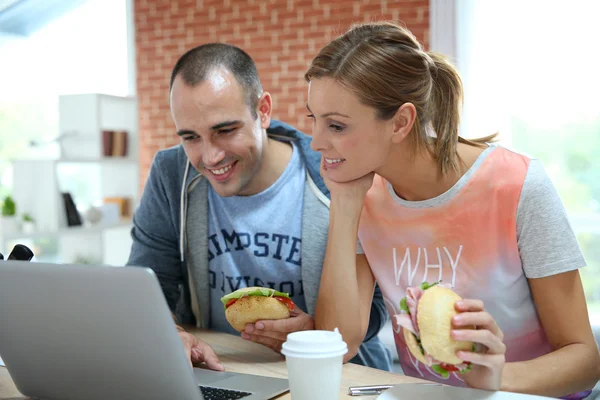 Colegas de quarto comendo sanduíche na frente do laptop — Fotografia de Stock