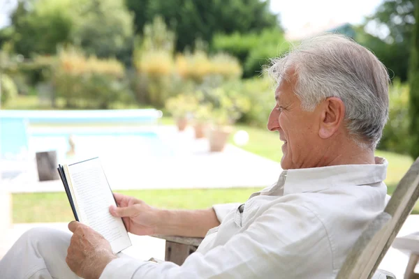 Uomo lettura libro in sedia a sdraio piscina — Foto Stock