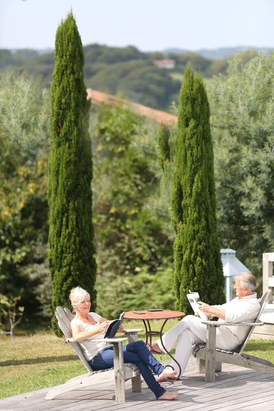 Paar in achtertuin lezen in ligstoelen — Stockfoto