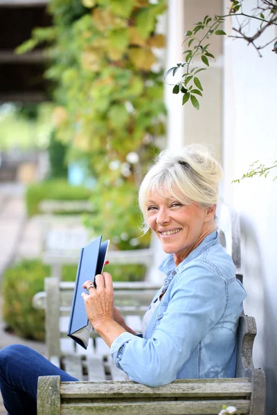 Senior woman reading book on bench — Stock Photo, Image