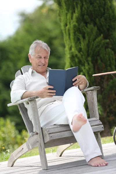Hombre leyendo libro en silla de la cubierta de la piscina — Foto de Stock