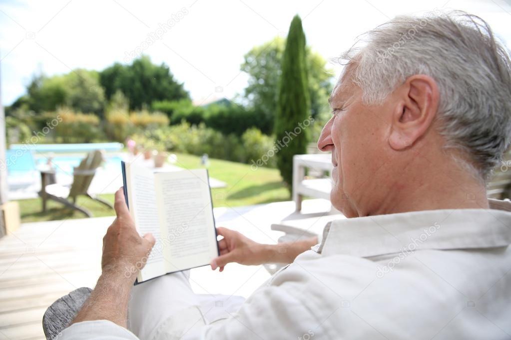 Man reading book in pool deck chair
