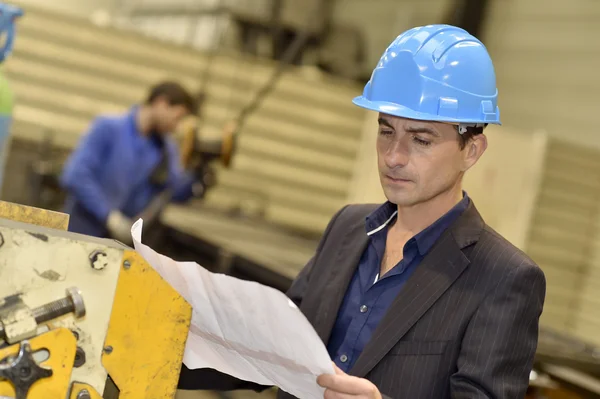 Engineer in factory reading blueprint Stock Picture