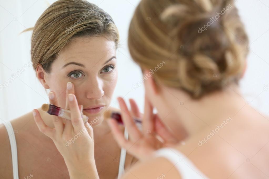 Woman applying concealer around eyes