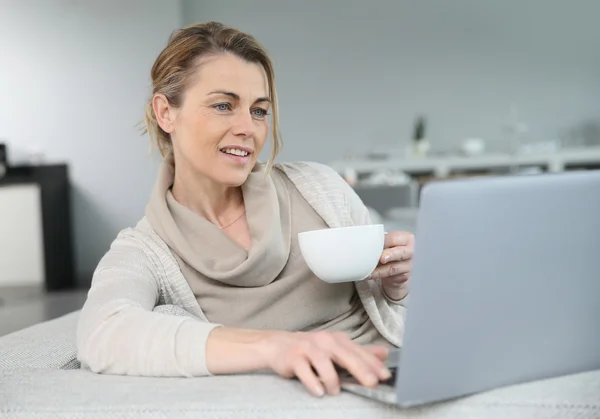 Kvinna med kaffe framför laptop — Stockfoto