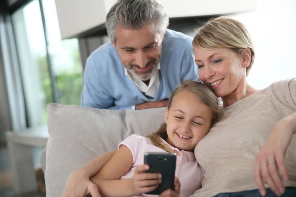 Родители смотрят, как дочь играет со смартфоном — стоковое фото