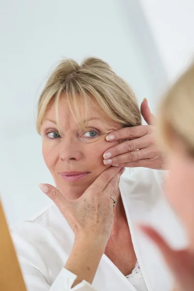 Seniorin schaut auf ihre Haut — Stockfoto