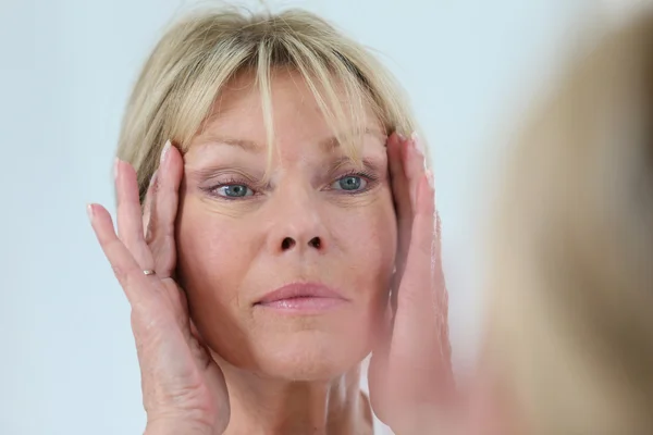 Vrouw kijkt naar haar huid in spiegel — Stockfoto