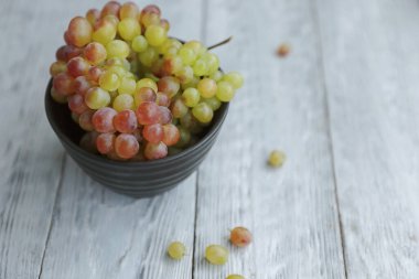Gri ahşap bir masada siyah bir kasede renkli üzümlerle dolu bir hayat..
