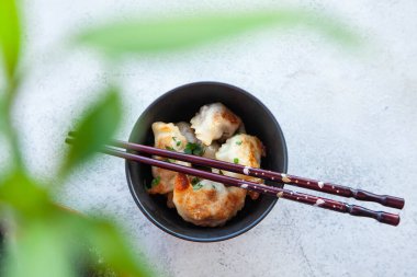 Kızarmış hamur köftesi ve Japon çubuğu ile siyah kase. Fotokopi alanı olan gri taştan bir zemin üzerinde Asya geleneksel yemeği.